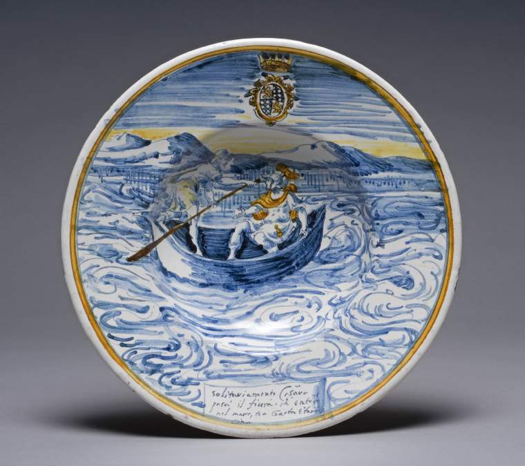 An image of Maker : Leonardo di Antonio Bettisi (workshop) Description: Renaissance maiolica broad-rimmed bowl . Painted in blue, yellow and orange with Caesar crossing a river in a boat.Technique :  Earthenware, tin-glazed overall. Size : diameter: (whole): 24.8 cmDate  : circa 1576