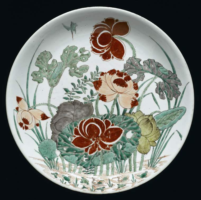 An image of Description: Saucer dish. Hard-paste porcelain painted in an enamel palette of two iron-reds, two greens, turquoise, pale yellow and aubergine outlined in sepia with a kingfisher in flight by a lotus pond with two mandarin ducks swimming.Saucer dish. Hard-paste porcelain painted in an enamel palette of two iron-reds, two greens, turquoise, pale yellow and aubergine outlined in sepia. The well rounded sides have an out-curved rim resting on a low tapered foot. The interior is boldy decorated with an overall design of a kingfisher diving down towards a large clump of lotus with six open blooms, flanked by frilly-edged leaves and tall water grasses, rising from a pond indicated by iron-red dashes, with two mandarin ducks swimming in the foreground. The base has two concentric circles in underglaze blue enclosing the mark. Production Place: China (country) Dimensions: diameter: (whole): 39 cm Period : Qing Dynasty (1644-1912), Kangxi Period (1662-1722) Date: circa 1662 to 1722   