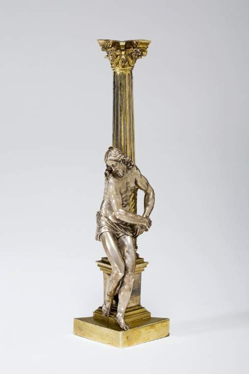 An image of Sculpture/Figure. Christ at the Column. Della Porta, Guglielmo, after (Italian architect, sculptor and restorer; born Porlezza between 1500 and 1510; died Rome, 1577). The column, cut in half diagonally, is hollow. It is fluted with a degenerate Corinthian capital with a winged cherub's head centrally placed between the corner volutes. On the abacus is a rosette above the cherub's head. Two-thirds of the way down the column the fluting is replaced by large acanthus leaves springing from the base mouldings and carved in relief. The column stands on a plinth, which is plain. Against this column, his body turned in contraposto, leans the figure of Christ, his manacled wrists held out to the right of his hips. His body, naked except for a loin-cloth, is highly modelled and is slightly doubled up as if to protect itself from the blows. The bearded face is turned down to the left, his hair falling in ringlets on his shoulders. The remains of a halo can be seen on the crown of his head. Silver alloy, parcel-gilt, the figure and column cast separately, c.1600-1700. Rome, Italy. Renaissance.