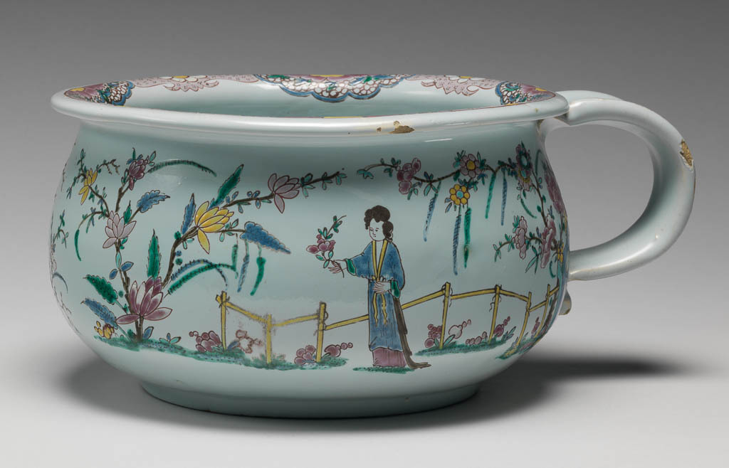 An image of English Delftware. Chamber Pot. Unidentified Liverpool pottery. Unidentified decorator, decorator, north Staffordshire. Circular with curved sides, and a loop handle on one side. Decorated on the outside with Chinese ladies among flowering plants, with rocks, a fence, and a Chinese style floral border. The inside is decorated with a floral spray. Buff earthenware, thrown with applied handle, tin-glazed greenish-white, and painted overglaze in enamels, height, whole, 11 cm, width, whole, 24 cm, circa 1750-1760. Chinoiserie. Famille Rose.