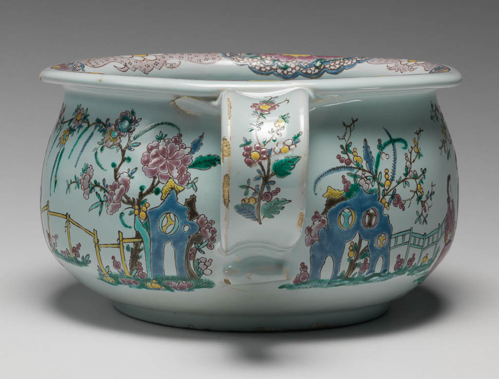An image of English Delftware. Chamber Pot. Unidentified Liverpool pottery. Unidentified decorator, decorator, north Staffordshire. Circular with curved sides, and a loop handle on one side. Decorated on the outside with Chinese ladies among flowering plants, with rocks, a fence, and a Chinese style floral border. The inside is decorated with a floral spray. Buff earthenware, thrown with applied handle, tin-glazed greenish-white, and painted overglaze in enamels, height, whole, 11 cm, width, whole, 24 cm, circa 1750-1760. Chinoiserie. Famille Rose.