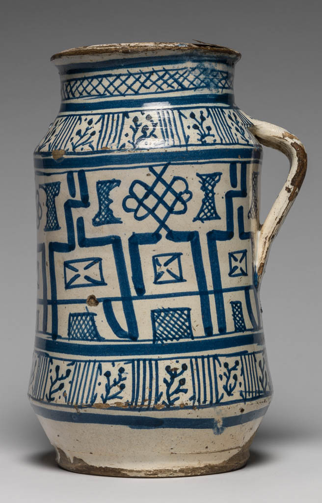 An image of Maiolica. Pharmacy Jar. Unknown maker, probably Florence. Albarello, with sloping shoulders, cylindrical neck with slightly everted rim, and, on one side, a small strap handle. Round the sides between horizontal bands, is a broad zone of geometrical ornament comprising debased Kufic, knots and cross-hatched rectangular and irregular shapes. On the shoulder and round the lower part of the jar there are groups of vertical strokes alternating with stylised plants; on the neck, trellis pattern between horizontal bands. Buff earthenware, tin-glazed on both sides, the interior now pale beige; base unglazed. Painted in blue. Height, whole, 24.5 cm, diameter, rim, 11.2 cm, diameter, base, 11.4 cm, width, whole, 16.0 cm, circa 1440-1460. Renaissance.