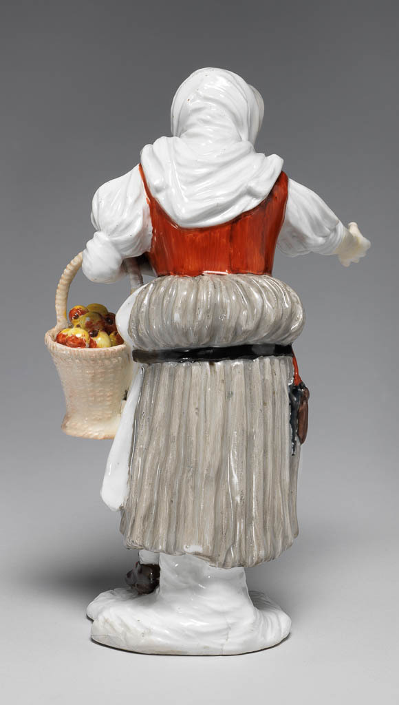 An image of Peasant woman selling apples. Meissen Porcelain Manufactory, Saxony. Kaendler, Johann Joachim, modeller (German, 1706-1775). Hard-paste porcelain, press-moulded, and painted overglaze in enamels, height, whole, 17.8 cm, width, whole, 11 cm, width, base, 6.2 cm, circa 1744-1750. Baroque. Over her left arm she carries a tall pale brown wicker basket full of yellow apples tinged with red, and with her right hand she proffers a single apple. Her head is wrapped a white shawl, which hangs half way down her back, and is knotted under her chin. Her face is haggard with strongly delineated black eyebrows, and red lips. She wears a white blouse with full elbow-length sleeves; a red bodice with a black front; a greyish-buff skirt bunched up around her buttocks by means of a black belt, from which dangle a black key and a brown sheath, hanging on a red strap; a white apron; white stockings; and brown shoes with red bows.