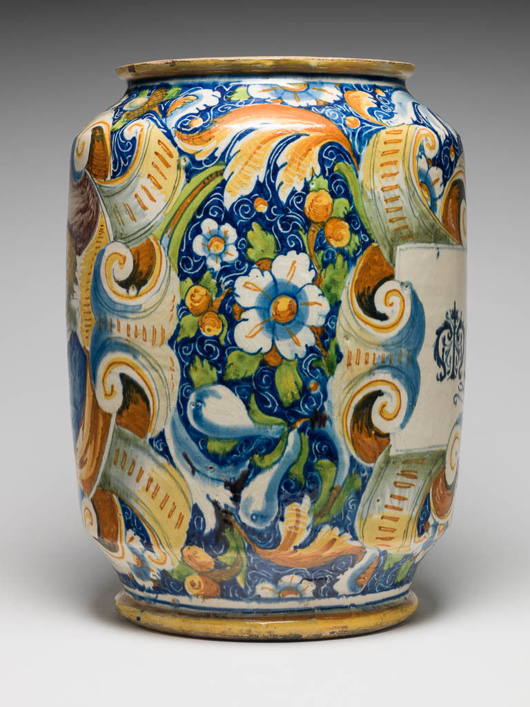 An image of Maiolica. Pharmacy jar/storage jar. Domenego da Venezia, workshop, The Veneto. On the front is a rectangular label inscribed `Mostarda FA' in blue gothic script, and framed by scrolls with a face at bottom centre. On the other side, within an oval scrolled frame, is a bust of a young man in profile to left, wearing a doublet, ruff and a soft rounded hat. The rest of the main field is decorated with stylised flowers, fruits, acorns and scrolling foliage, reserved in a blue ground incised with coiling tendrils. Earthenware, thrown, tin-glazed on the exterior and interior; rim and base unglazed, painted in polychrome, height, whole, 39.5 cm, diameter, rim, 21.5 cm, diameter, base, 22.0 cm, width, widest part, 28.9 cm, circa 1560-1570. Renaissance.