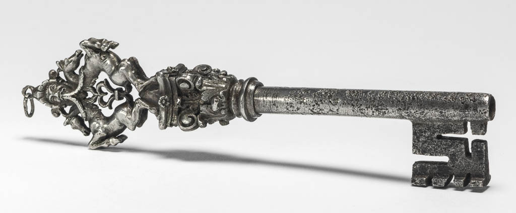 An image of Key. Iron, with piped stem, collar in the form of a Corinthian capital and bow composed of two prancing horses back to back surmounted by a mask, at the top, a ring for suspension. Circa 1500-1600. French.