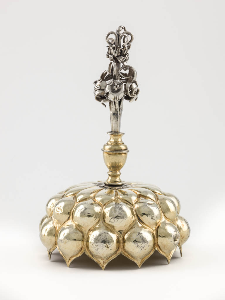 An image of Cup and cover/pineapple cup. Fischer, Franz (silversmith, Nüremberg, surname is also spelt Vischer). Lobed ovoid body and cover supported by a stem in the shape of a tree trunk with figure of a woodman. Silver-gilt; the spreading circular silver-gilt foot is embossed with a ring of lobes round a central dome, which supports the silver stem in the shape of a tree trunk encircled by a creeper, and the figure of an ax-wielding woodman. The ovoid silver-gilt body and interlocking cover are embossed with lobes. The silver finial is formed as a bunch of flowers. Silver and gold, raised and embossed body and foot, cast stem and woodcutter, height, overall, 33.3 cm, diameter, overall, 8 cm, weight, whole, 281 g, 1600-1653. Mannerist.
