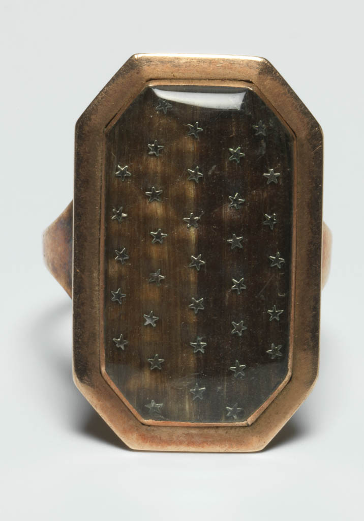 An image of Jewellery. Ring/Mourning Ring. Gilt-metal, plain, narrow hoop, broadening at shoulders. Long octagonal bezel, containing under glass, hair of two different colours set with rows of small metal stars. Inscribed on the back: 'NB Toms Ob 19 Dec 1794 At 5ys W: Toms ob: 28 Mars 1786 Aet 11 ys'. Height, hoop, 1.5 mm, depth, hoop, 1.0 mm, length, hoop, 21.0, mm, height. bezel, 27.0 mm, length, bezel, 17.0 mm, width, bezel, 4.5 mm, 1786. English.