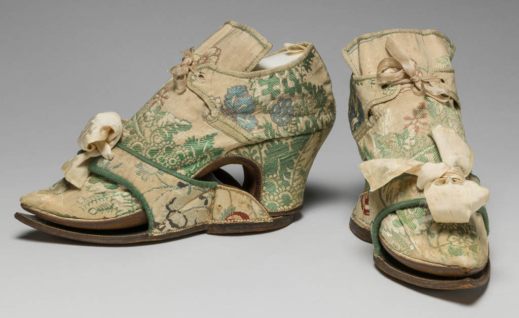 An image of Textiles/Shoes and pattens. Brocaded silk, cream background, multicoloured floral design. Shoes lined with coarse linen, tongues with green sarcenet, bound green braid. Pattens lined scarlet flannel, bound green braid, cream corded silk bows, leather soles and heels. Length, whole, 8.25 in, circa 1700-1749. English.