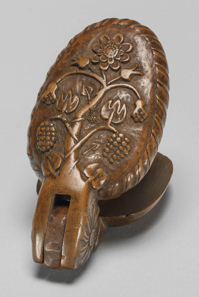 An image of Cutlery/Spoon/Flatware. Folding, in the form of two hinged oval bowls. The back of the one used as a handle is carved with a tree with stylised flowers and fruit within a gadroon border; the inside is deeply carved as a woman on horseback. The wood was carved in two pieces which were joined with a hinge. Fruit wood, length, overall, 14.5 cm, circa 1650-circa 1700. German.