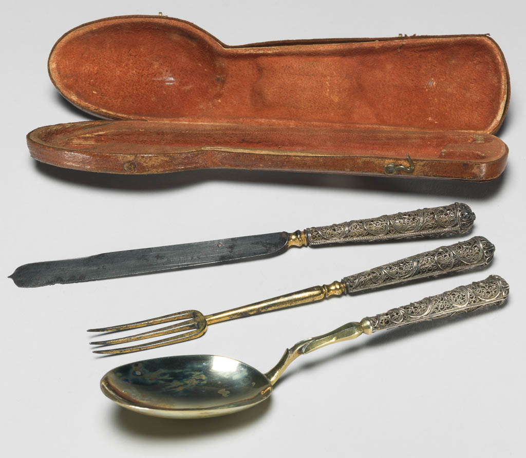 An image of Cutlery Set. Knife, fork, spoon and case. Laminet, Johann Christoph, spoon maker, attributed, Augsburg. Unidentified cutler. Unknown handle maker. Silver, parcel-gilt and steel, leather with gilt tooling; the knife (A) has a steel blade which flares towards its rounded end with central point; the baluster shaped bolster is gilt; the silver handle is circular in section and broadens towards the terminal cap; the sides are of open filigree scrolls between two rope borders. The fork (B) has three gilt metal tines on a long knopped stem. The spoon has an oval silver-gilt bowl with a rat-tail on the back. Both the fork and spoon have handles which are similar to that of the knife. The case (C) has a hinged lid and is approximately the shape of a spoon with a broad handle. It is covered with red leather with tooled partially gilt decoration. Length, knife, 17.7 cm, length, fork, 15.4 cm, length, spoon, 15.7 cm, length, case, 19.3 cm, circa 1695- circa 1707. German.
