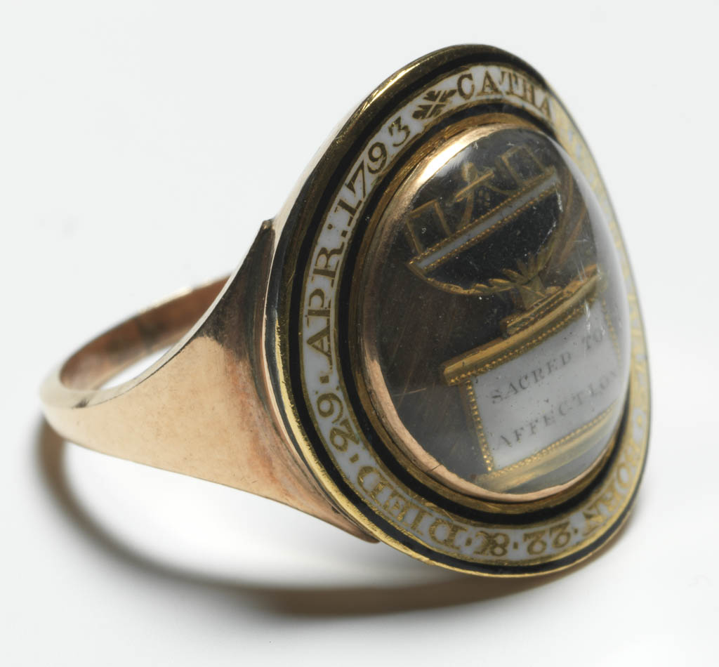 An image of Jewellery/Mourning ring. Gold hoop, expanding at shoulders. Circular bezel. Round the edge, reserved in white enamel, bordered at both edges with a narrow band of black enamel, is in the inscription: CATHERINE. HARRIS. BORN 22. 8C. DIED. 29. AP: 1793. At the centre, under glass, on a background of hair, an urn on a pedestal, inscribed 'SACRED TO AFFECTION'. Urn composed of gilt-metal, black and white enamel. Gold, hair, enamel and gilt-metal, height, hoop, 2.0, mm, depth, hoop, 1.25, mm, length, hoop, 21.0, mm; height, bezel (circular) 5.0 mm, length, bezel (circular) 20.0, mm, width, bezel (circular) 20.0 mm, 1793. English.
