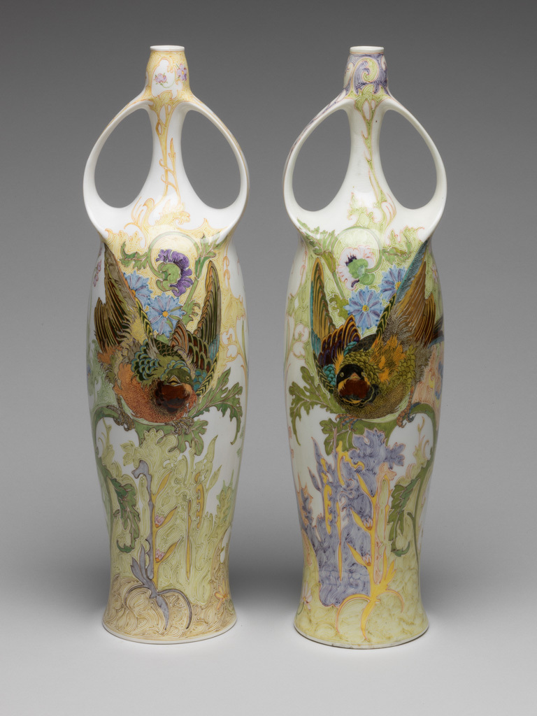 An image of Pair of two-handled balaster vases. Tegel en Fayencefabriek Amphora Factory, Oegstgeest. Designed by J. Jurriaan Kok (Dutch, 1861-1919). Painted by Samuel Schellink (Danish, 1876–1958). C.28-2014: Tall eggshell porcelain vase, baluster shape, hand-painted in polychrome enamels with bird, poppy and foliage motifs in Art Nouveau style. Circular in plan, with tall gently-concave body rising to a long narrow neck, the top of the neck slightly wider than the bottom. Two strap handles, cast with the body, rise from the shoulders and rejoin the vase towards the top of the neck. The overall form suggests an erect female body with arms raised to her head. Decorated with a finely painted flowing floral design. On one side is a green-headed songbird which appears to be flying out of the body. On the other side is a large spray of purple and light blue oriental poppies. Eggshell porcelain, decorated underglaze in polychrome enamels with hand-painted motifs, height 36.5 cm, base width 8.5 cm, circa 1914.C.29-2014: Tall eggshell porcelain vase, baluster shape, hand-painted in polychrome enamels with bird, poppy and foliage motifs in Art Nouveau style. Circular in plan, with tall gently-concave body rising to a long narrow neck, the top of the neck slightly wider than the bottom. Two strap handles, cast with the body, rise from the shoulders and rejoin the vase towards the top of the neck. The overall form suggests an erect female body with arms raised to her head. Decorated with a finely painted flowing floral design. On one side is a black-headed songbird which appears to be flying out of the body. On other side is a large spray of orange oriental poppies. Eggshell porcelain, decorated underglaze in polychrome enamels with hand-painted motifs, height 36.5 cm, base width 8.5 cm, circa 1914.