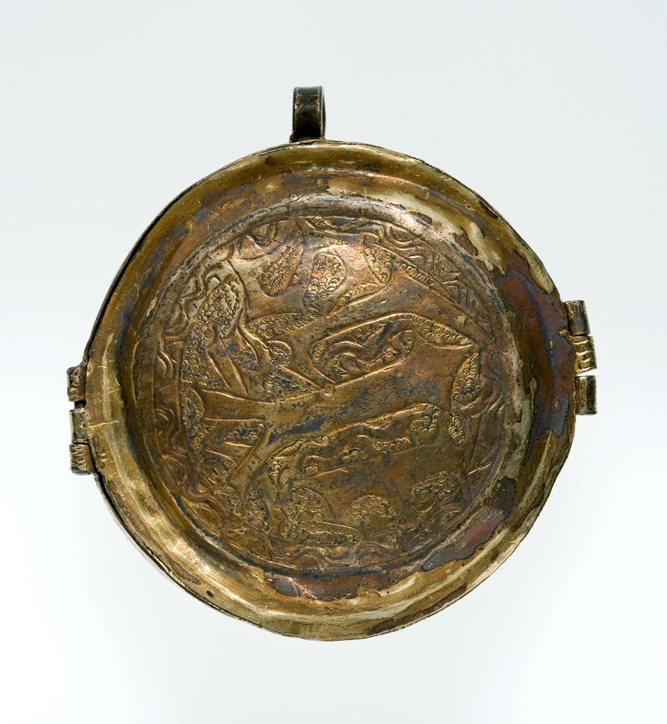 An image of Boxes/Pyx. Church Plate. Sacramental wafer box or reliquary (possibly). Circular with straight sides and slightly domed base and hinged cover. Sacred Monograms are chased on the lid, 'IHS', and the base 'XPS'; both are on a punched scale-work ground and within a chased wavy border. On the opposite side to the hinge is a simple catch of similar form to the hinge with three knuckles. Set at right-angles to the hinge and catch a ring is soldered to the side. Siver-gilt, punched and chased, height 2.6 cm, length 7.6 cm, width 7.2 cm, 1500-1525.