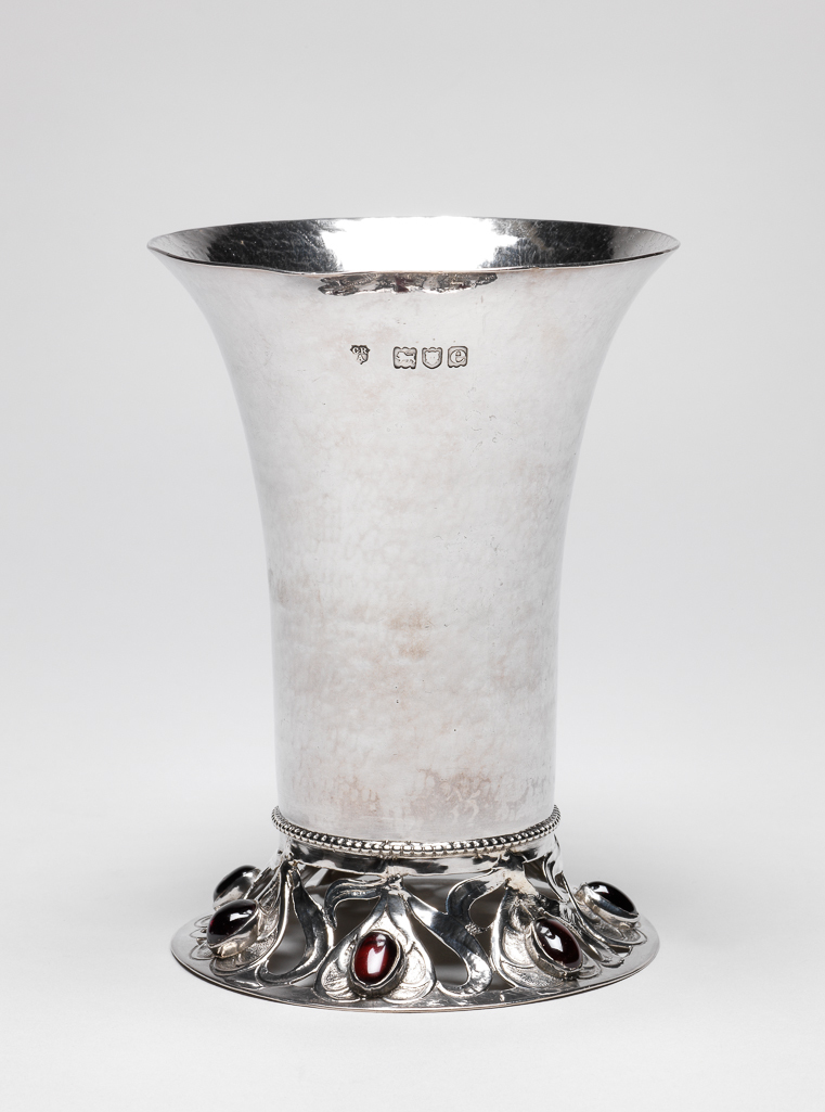 An image of Silverware. Beaker/Drinking Vessel. Ashbee, Charles Robert (British, 1863-1942). Silver beaker with hammered surface, the foot pierced, chased, and set with unbroken amethysts. Maker’s mark of C.R. Ashbee and London hallmarks. After 1900 to before 1901. Acquisition Credit: Given by the estate of the late Olive and Peter Ward. Former loan number; AAL.6-2005.