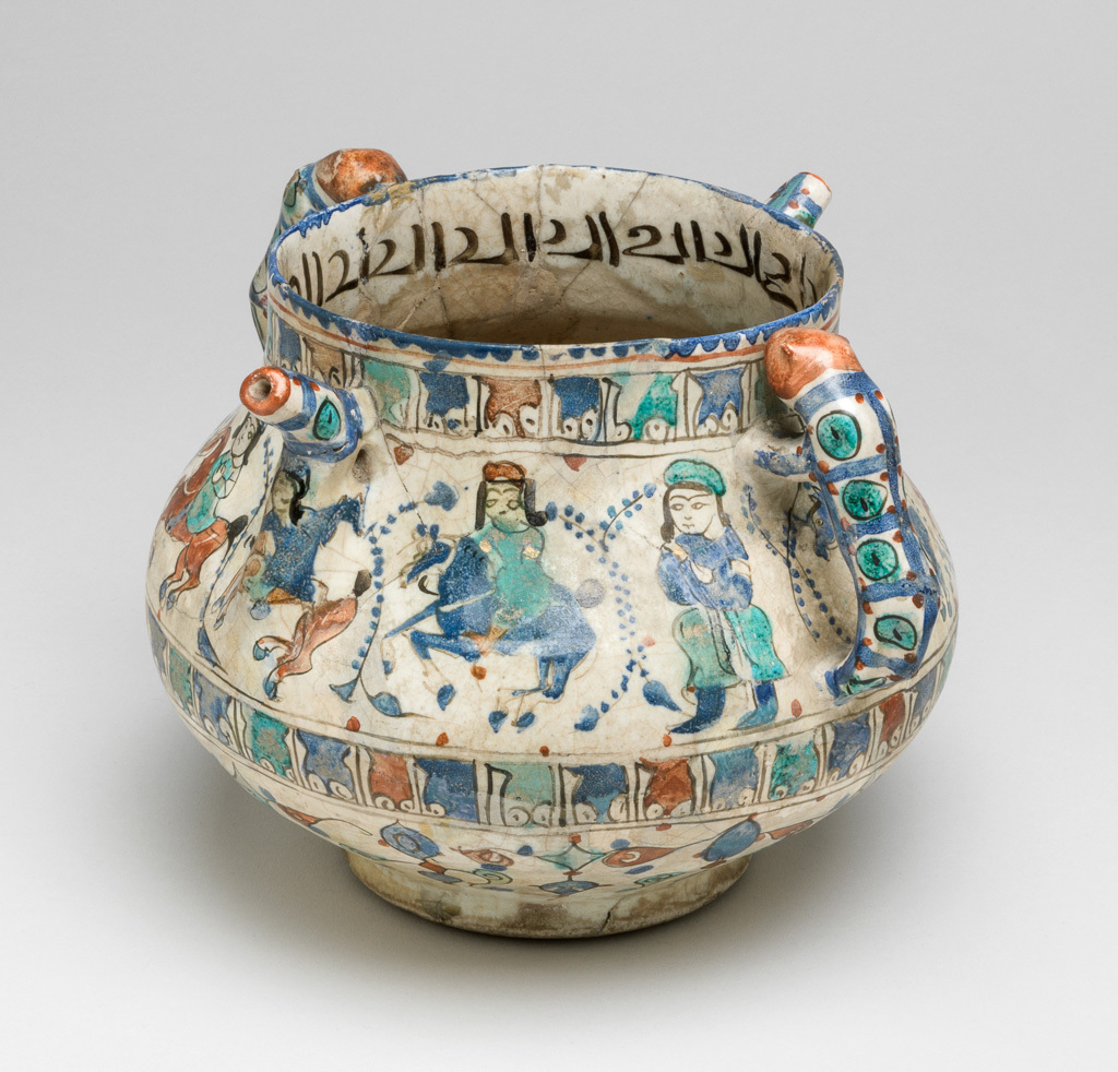 An image of Posset pot/spouted jar. Islamic pottery, Minai. Unknown, potter, probably Kashan. Shape: bulbous body with a cylindrical neck and plain rim, sitting on a low foot ring. Opposing cheetah handles and angular spouts are attached to the upper body. Exterior: the rim is painted with a blue dentilated pattern. On the upper body, a frieze of mounted horsemen and two standing figures each separated by feather-like foliage, are identically dressed in hats, tunics, and leggings, occasionally wearing golf leaf arm bands. This frieze is delineated above and below by narrow bands of Arabic script, possibly pseudo epigraphic. On the lower body, a frieze of alternately transposed triangular floral garlands is painted. All these friezes are outlined in black and coloured with blue, turquoise, red and black. Two lion shaped handles, with red heads and bodies decorated with blue stripes and turquoise and red dots, are joined to the upper body. White glaze runs unevenly over the lower body and in places onto the foot ring. Interior: blue paint continues on the rim, while on the neck black Arabic script (cursive) is painted. Remainder is undecorated except for a covering of white glaze. Fritware, wheel thrown body and moulded handles and spout, coated in an opaque white, slightly crazed glaze; decorated with blue and turquoise in-glaze painting, black and red overglaze painting and gilding. Height, whole, 14.5 cm, width, whole, 17.4 cm, diameter, rim, 11.3 cm, diameter, base, 8.9 cm, weight, whole, 708 g, circa 1180-1219. Seljuk Period.