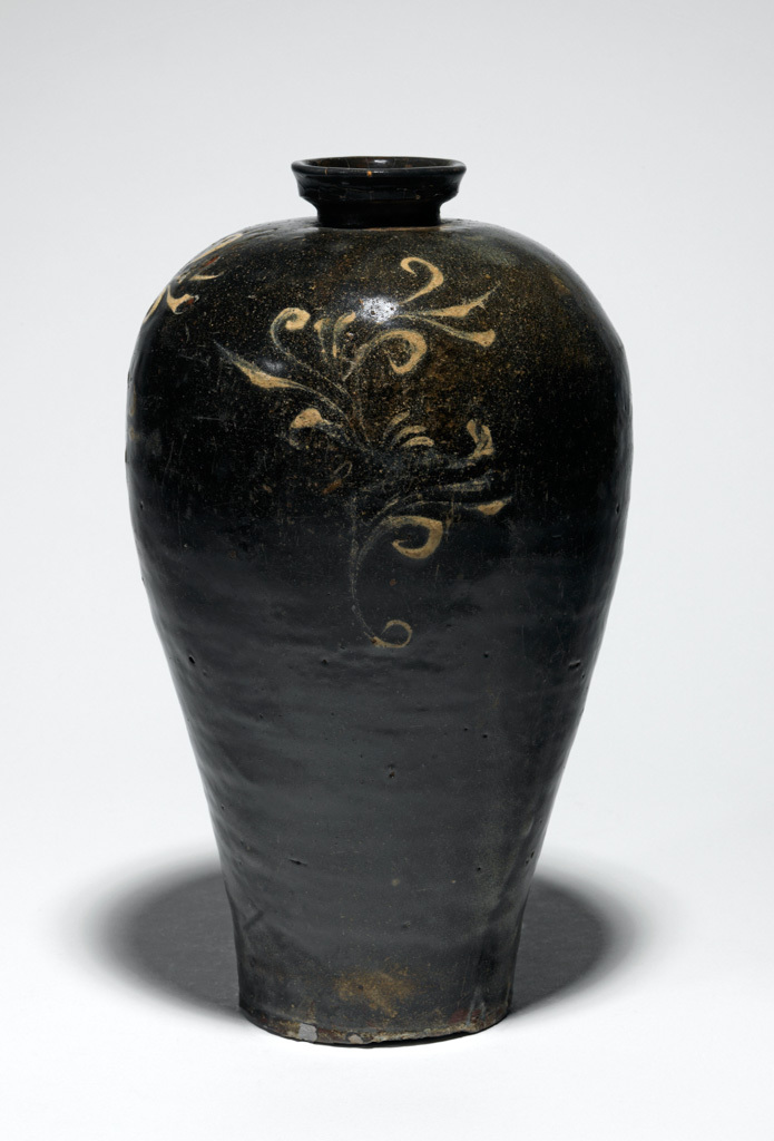An image of Maebyong vase with foliage design. Unknown pottery, South Cholla province, Haenam-gun, Chinsan-ri kilns. The maebyong-shaped vase has a short neck with a (replaced) cup-shaped mouth, its sides gently tapering from the rounded shoulder to the slightly spread base, with a low curved footring. The whole vessel is covered with iron-oxide onto which three foliage motifs have been painted in white slip. The slip has in places been thickly applied, almost giving the impression of a relief design. A glossy pale green celadon glaze with a fine crackle has been thinly applied on top. The glaze has pooled towards the base, which is mainly unglazed and has fired a reddish colour; the footring shows traces of fire-clay spurs. Stoneware, thrown, washed with iron-oxide, painted in white slip and celadon-glazed, height 26.5 cm, diameter, rim, 5.3 cm, diameter, foot, 8.5 cm, circa 1050-1150. Koryo Dynasty. Production Note: This type of maebyong was used as a wine vessel, and was made in the kilns at Chinsan-ri, Haenam-gun, South Cholla province, in the second half of the eleventh or first half of the twelfth century.