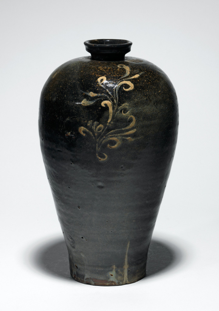 An image of Maebyong vase with foliage design. Unknown pottery, South Cholla province, Haenam-gun, Chinsan-ri kilns. The maebyong-shaped vase has a short neck with a (replaced) cup-shaped mouth, its sides gently tapering from the rounded shoulder to the slightly spread base, with a low curved footring. The whole vessel is covered with iron-oxide onto which three foliage motifs have been painted in white slip. The slip has in places been thickly applied, almost giving the impression of a relief design. A glossy pale green celadon glaze with a fine crackle has been thinly applied on top. The glaze has pooled towards the base, which is mainly unglazed and has fired a reddish colour; the footring shows traces of fire-clay spurs. Stoneware, thrown, washed with iron-oxide, painted in white slip and celadon-glazed, height 26.5 cm, diameter, rim, 5.3 cm, diameter, foot, 8.5 cm, circa 1050-1150. Koryo Dynasty. Production Note: This type of maebyong was used as a wine vessel, and was made in the kilns at Chinsan-ri, Haenam-gun, South Cholla province, in the second half of the eleventh or first half of the twelfth century.