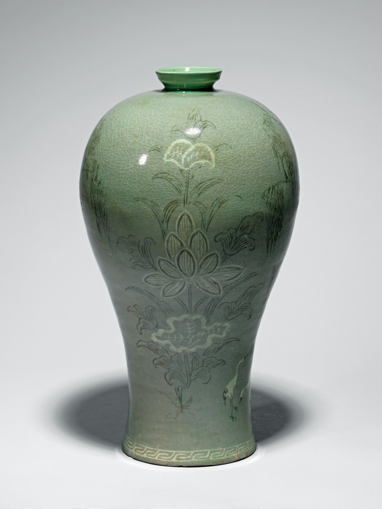 An image of Maebyong. Unknown, probably North Cholla province, Puan-gun, Yuch'on-ri kilns. Vase with willow trees, cranes and lotus design. This maebyong-shaped vase has a wide shoulder and a narrow base and rests on a broad low footring. The neck has been restored. The body is inlaid in black and white slip with two large lotus sprays with fully opened blooms, between painterly scenes of cranes under a willow tree. Around the base is a band of key-fret in white slip. The glaze is of opaque pale bluish-green tone, glossy, and with a fine crackle. The glaze has been wiped from the footring, which shows traces of ten fire-clay spurs. Stoneware, thrown, inlaid in black and white slip, and celadon-glazed, height, whole, 34.6 cm, diameter, rim, 5.7 cm, diameter, foot, 12.2 cm, circa 1200-1250. Koryo Dynasty. Production Note: This type of maebyong was used as a container for fine wine, made from plum flowers or ginseng. It originally probably had a cover.
