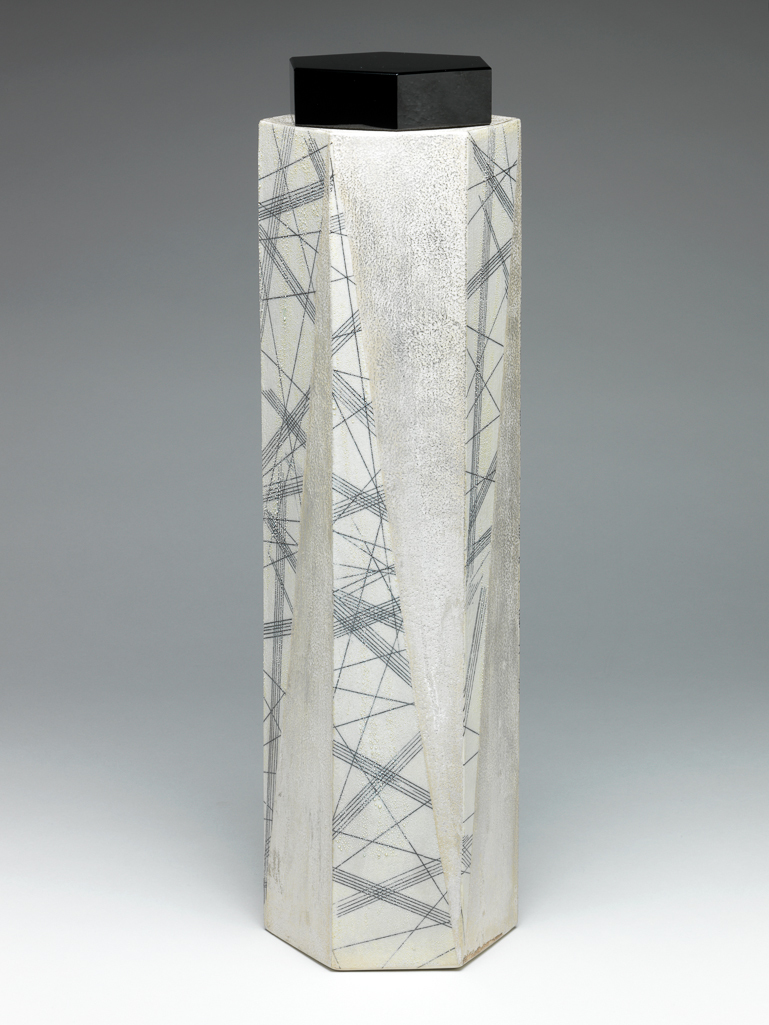 An image of Studio Ceramics. Black and White Mist Tall Box. Takahiro, Kondo (Japanese, b.1948). The sides of the box are decorated with elongated silver-grey triangles alternating with wider white triangles crossed by black lines and scattered with silver globules. The interior is black. Porcelain with gintekisai (silver mist) over-glaze and a black cast glass lid, height, whole, 47.7 cm, height, box to shoulder, 44.5 cm, width, base across points, 14.1 cm, height, cover, 4 cm, width, cover across points, 11.5 cm, circa 2007. Kyoto, Japan. Gift of Nicholas and Judith Goodison through The Art Fund.