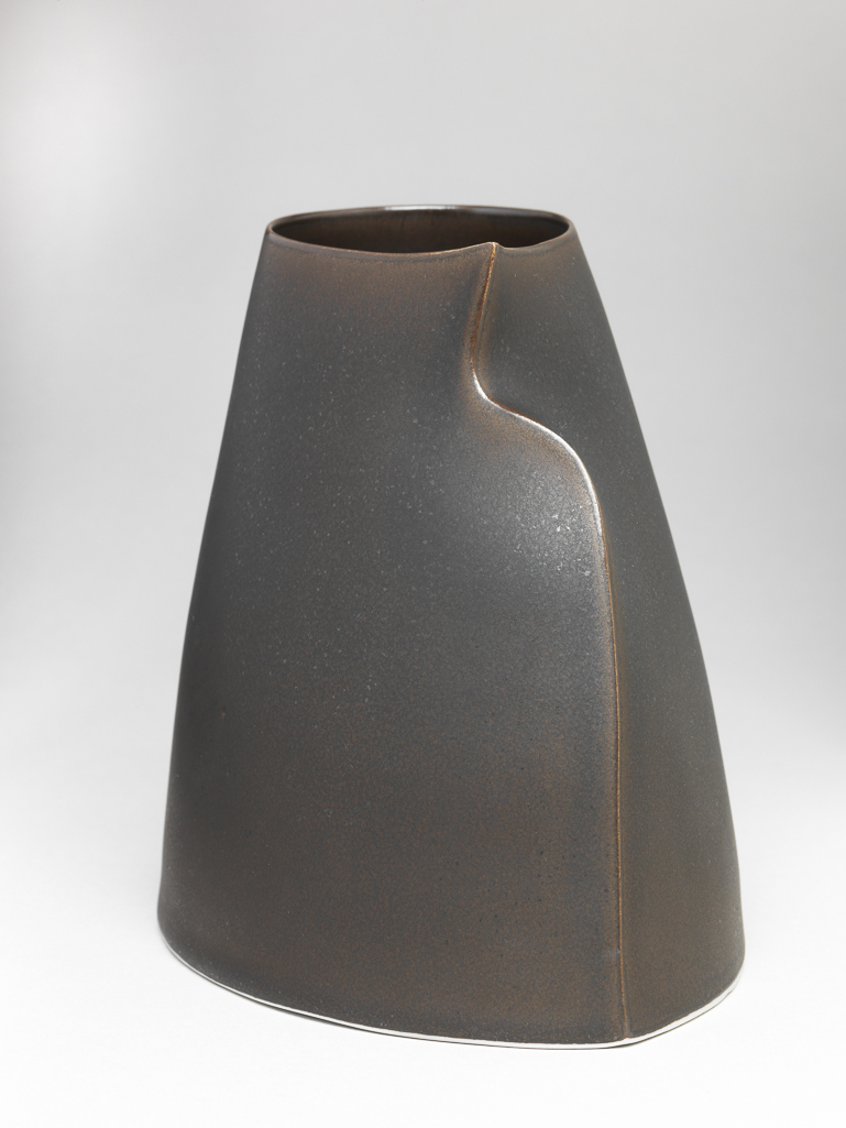 An image of Studio Ceramics. Esker Vessel. Flynn, Sara (Irish, b.1971). Short vessel with teardrop-shaped opening at the top. The thrown vessel has been squeezed to form a sharp spine from the point of the teardrop to the base. Spray glazed inside and out to give a bronze-like surface. The underside is flat and unglazed. White porcelain, thrown and altered, spray glazed and polished. Height, 14 cm, width, 15.5 cm, depth, 11 cm,  circa 2013. Acquisition Credit: Gift of Nicholas and Judith Goodison through The Art Fund.