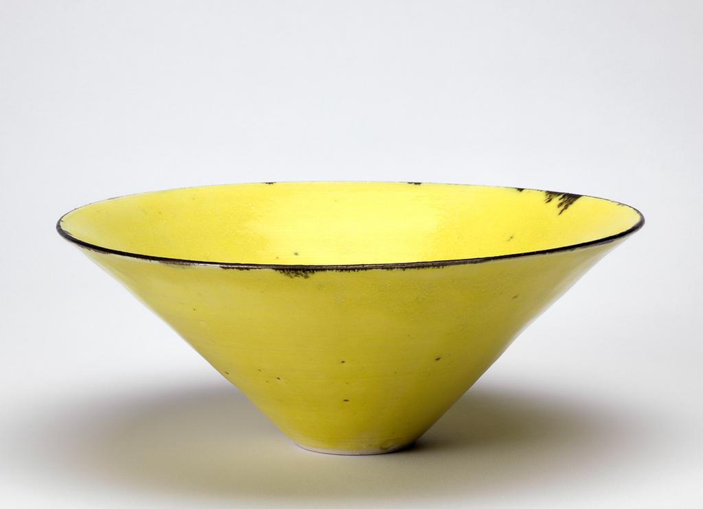 An image of Studio Ceramics. Contemporary Craft. Bowl. Cooper, Emmanuel (British,  1938-2012). Porcelain, thrown, with yellow glaze, random gold spots, and metallic glazed rim which has dribbled downwards a little here and there; foot ring unglazed. Circular with deep sides rising from a narrow recessed base. Height, whole, 10 cm, diameter, whole, 25.2 cm, 2004. Acquisition Credit: Gift of Nicholas and Judith Goodison through the National Art Collections Fund.