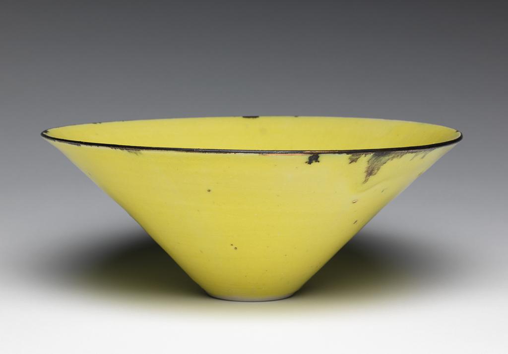An image of Studio Ceramics. Contemporary Craft. Bowl. Cooper, Emmanuel (British,  1938-2012). Porcelain, thrown, with yellow glaze, random gold spots, and metallic glazed rim which has dribbled downwards a little here and there; foot ring unglazed. Circular with deep sides rising from a narrow recessed base. Height, whole, 10 cm, diameter, whole, 25.2 cm, 2004. Acquisition Credit: Gift of Nicholas and Judith Goodison through the National Art Collections Fund.