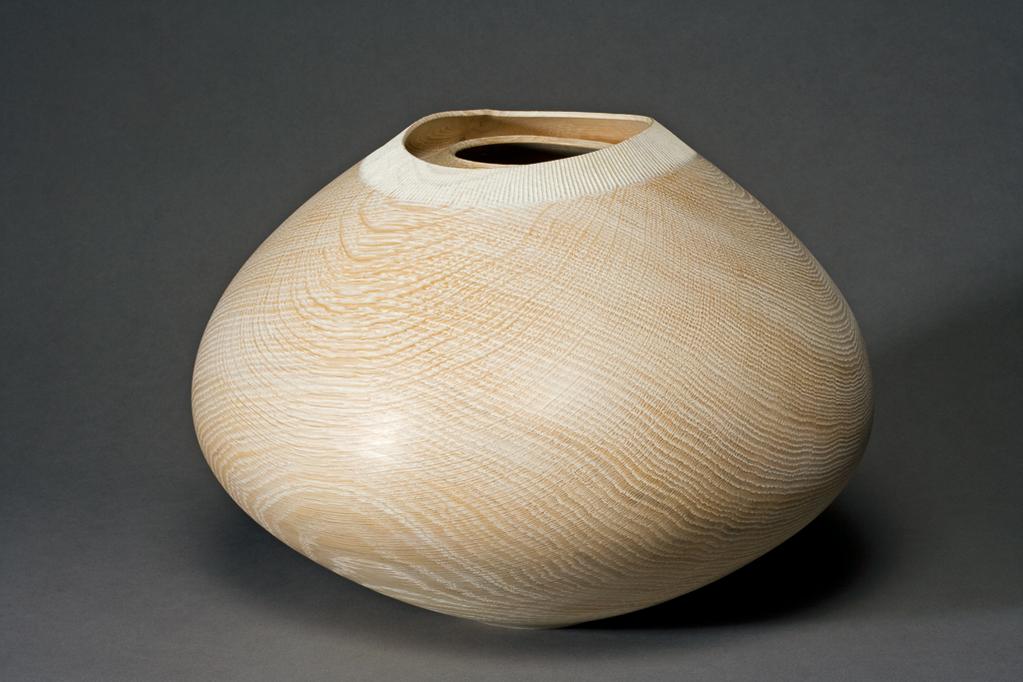 An image of Contemporary Craft. Inner Rimmed Vessel. Woodwork. Flynn, Liam (Irish). Of elongated ovoid form with a double rim, the outer one larger and a different shape from the inner one, which has a hole on one side under the outer rim. The edge of the outer rim is bordered by close-set carved striations. On one side of the exterior there is a subsantial knot in the wood. Irish oak, turned and carved, height, whole, 27 cm, width, whole, 36.7 cm, made before 25 January 2008. Gift of Nicholas and Judith Goodison through The Art Fund.