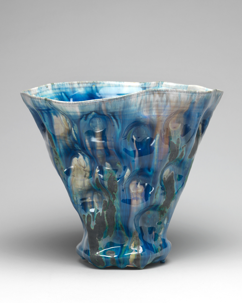 An image of Contemporary Craft. Studio Ceramics. Vase. Tchelenko, Janice (British, b. 1942). The vase has a concave base, and sides which slope upwards and outwards to an irregularly shaped, roughly circular rim. The glazes are applied to produce a runny, variegated effect. High-fired reduced stoneware, thrown, dimpled, and squashed, and painted with blue, green, grey and brown glazes, except for the base, which appears to be coated in pale grey slip, height 24 cm, width 27.5 cm, dated 1997. Gift of Nicholas and Judith Goodison through the National Art Collections Fund.
