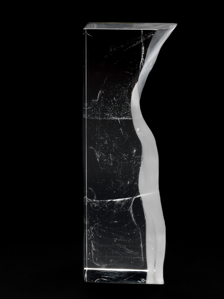 An image of Studio Glass. Aura VII Torso. Romanelli, Bruno (British, b.1968). A narrow rectangular pillar indented with the outline of a human torso with a nipple. The surface of the indentation is sandblasted. Within the glass there are various indeterminate misty markings. Clear glass, cast, sandblasted, and polished, height 41.5 cm, width, top, 14.5 cm, width, bottom, 13.1 cm, depth 9.9 cm, 1999. Gift of Nicholas and Judith Goodison through the National Art Collections Fund.