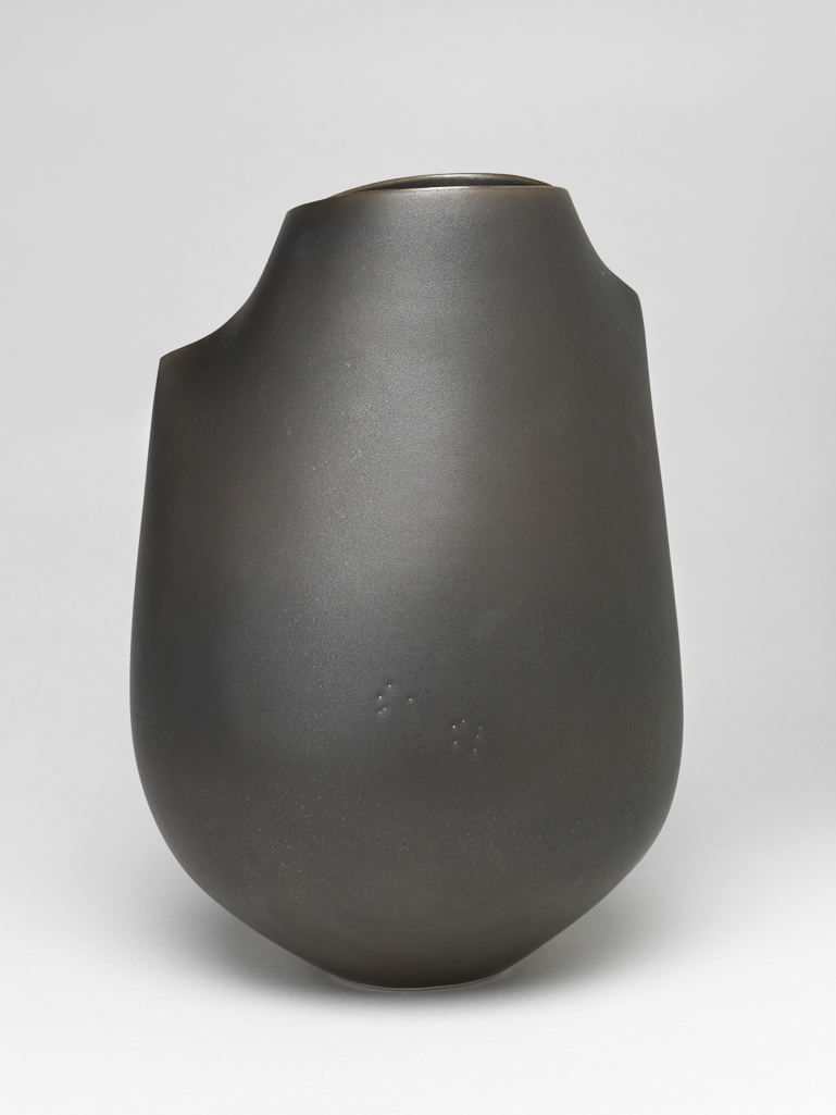 An image of Studio Ceramics. Double-Spine Camber Vessel. Flynn, Sara (Irish, b.1971). Tall vessel with reduced-size heart-shaped opening at the top. The upper part folded on either side of the opening to form a short spine and shoulder, the lower part retains its thrown form. Spray glazed inside and out to give a bronze-like surface. The underside is small, round, flat and unglazed. White porcelain, thrown and altered, spray glazed and polished. Height 23 cm, width 16.5 cm, 2014. Acquisition Credit: Gift of Nicholas and Judith Goodison through The Art Fund.