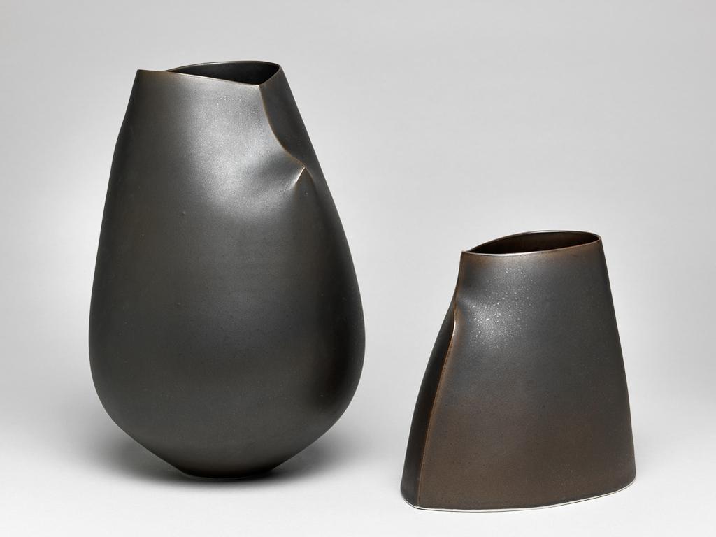 An image of Studio Ceramics. Double-Spine Camber Vessel. Flynn, Sara (Irish, b.1971). Tall vessel with reduced-size heart-shaped opening at the top. The upper part folded on either side of the opening to form a short spine and shoulder, the lower part retains its thrown form. Spray glazed inside and out to give a bronze-like surface. The underside is small, round, flat and unglazed. White porcelain, thrown and altered, spray glazed and polished. Height 23 cm, width 16.5 cm, 2014. Acquisition Credit: Gift of Nicholas and Judith Goodison through The Art Fund.