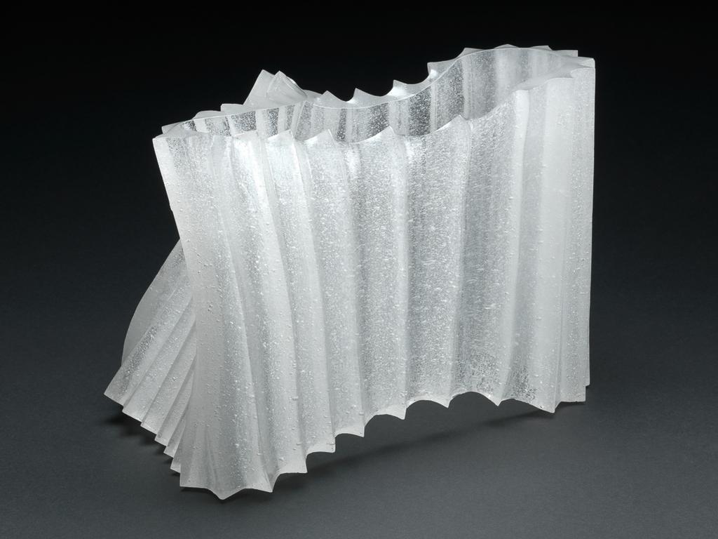 An image of Studio Glass. Contemporary Craft. Clear Glass Form. Sato, Naoko (Japanese, b.1964). Extremely bubbly glass, cast, and kiln formed by heat. Formed as a vertical pleated tube which has been manipulated into an irregular roughly rectangular shape, wider at one end than the other, and sloping inwards at the wider end. Height 21.5 cm, length 30 cm, width 16.5 cm, 1999. Gift of Nicholas and Judith Goodison through the National Art Collections Fund.