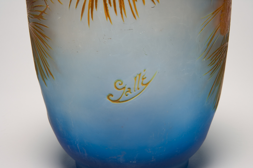 An image of Gallé, Emile (French, 1846-1904.) Glass vase cut with an assymetrical design of pine branches and cones. Blue blown glass, cased in orange and brown, and carved, height 27.0cm, diameter (whole) 16.6cm, circa 1890. French.