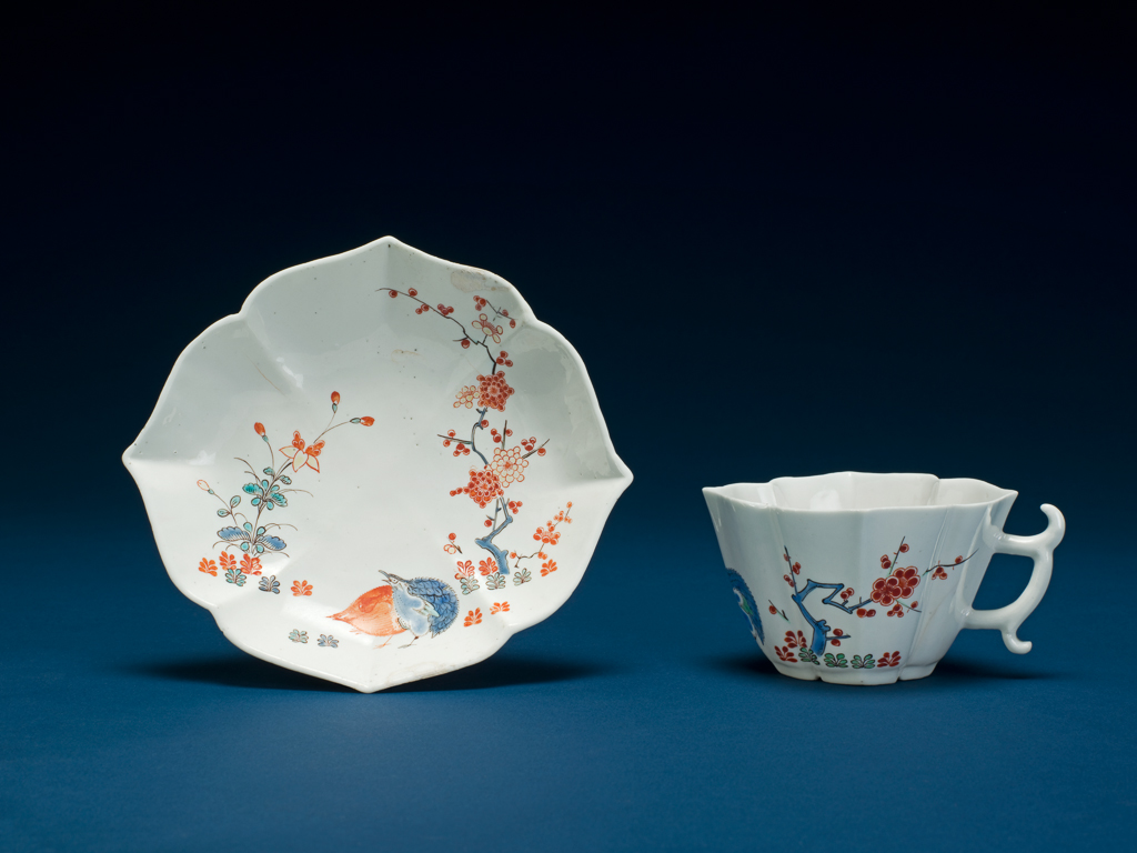 An image of Cup/saucer/teaware. Chantilly Porcelain Manufactory. Both pieces are of a cusped quatrefoil plan with bases divided into four by channels radiating from a central depression. The cup has an angular handle with two projecting scrolls. The outside of the cup and the inside of the saucer are decorated with 'Quail Pattern'. Soft-paste porcelain, moulded, covered with white tin-glaze, and painted in blue, green, yellow, red, and black enamels in Kakiemon style. Height, cup, 5 cm, width, cup, 9.7 cm, height, saucer, 2.6 cm, width, saucer, 13.3 cm, circa 1730-1735. Kakiemon style. Production Note: The 'Quail Pattern' was one of the most popular Japanese Kakiemon style designs and was copied by many European factories. The cusped quatrefoil forms of the cup and saucer were copied from Meissen models of about 1730.