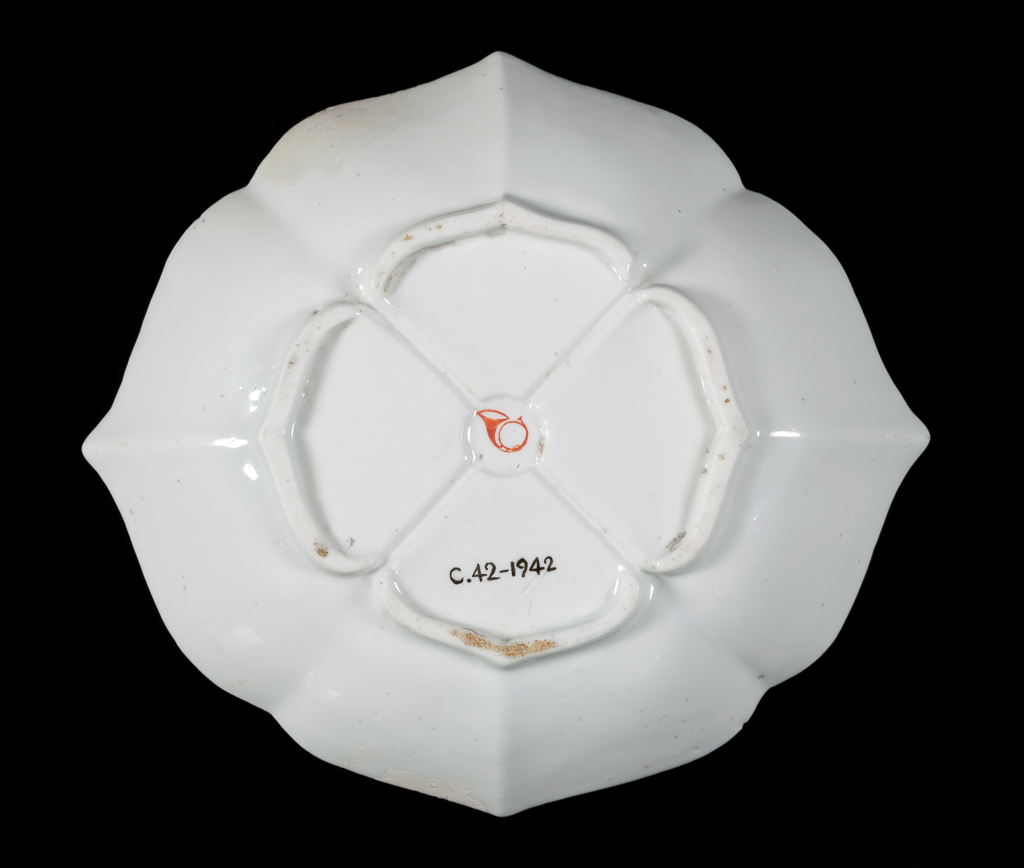An image of Cup/saucer/teaware. Chantilly Porcelain Manufactory. Both pieces are of a cusped quatrefoil plan with bases divided into four by channels radiating from a central depression. The cup has an angular handle with two projecting scrolls. The outside of the cup and the inside of the saucer are decorated with 'Quail Pattern'. Soft-paste porcelain, moulded, covered with white tin-glaze, and painted in blue, green, yellow, red, and black enamels in Kakiemon style. Height, cup, 5 cm, width, cup, 9.7 cm, height, saucer, 2.6 cm, width, saucer, 13.3 cm, circa 1730-1735. Kakiemon style. Production Note: The 'Quail Pattern' was one of the most popular Japanese Kakiemon style designs and was copied by many European factories. The cusped quatrefoil forms of the cup and saucer were copied from Meissen models of about 1730.