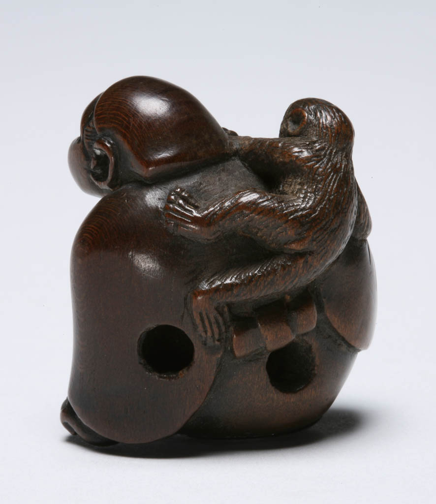 An image of Netsuke/katabori. Miwa, maker, Japan. A sarumawashi (monkey-trainer) clad in a robe, his head covered, seated and grimacing with pain as the monkey climbing on his back pulls at his right ear. He grasps the monkey's paw with his right hand as he tries to release the monkey's grip. Himotoshi at the back amid his robes. Dark wood, finely carved, height, whole, 3.9 cm, width, whole, 3.4 cm, circa 1700-1800. Edo Period (1615-1868).