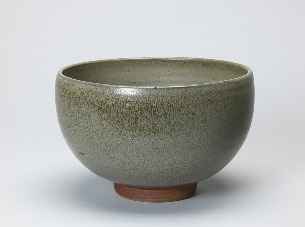 An image of Studio Ceramics. Bowl. Braden, Norah, probably (British, 1901-2001). Circular, with deep curved sides, inclining inwards slightly at the top, standing on a footring which is unglazed. Stoneware, thrown, and ash-glazed grey-green with brownish streaks and speckles, height 13.5 cm, diameter 21 cm, circa 1930-1936.
