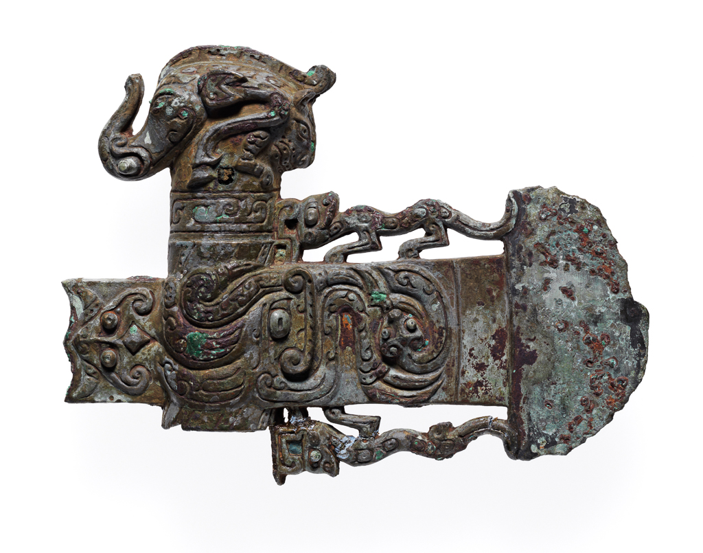An image of Axe head. The blade, socket, and socket cap all one piece of metal. The blade is flanked by two tigers. On the blade is a coiled dragon, a conventionalised dragon's head, and a t'ao t'ieh mask in the piece of blade at the back. On the cap is an elephant's head with horse's legs and a tiger's head at the back. Bronze, height 11.1 cm, length 14.6 cm, circa 500-249 B.C. Chou dynasty (1122-249 BC). Chinese Warring States period.