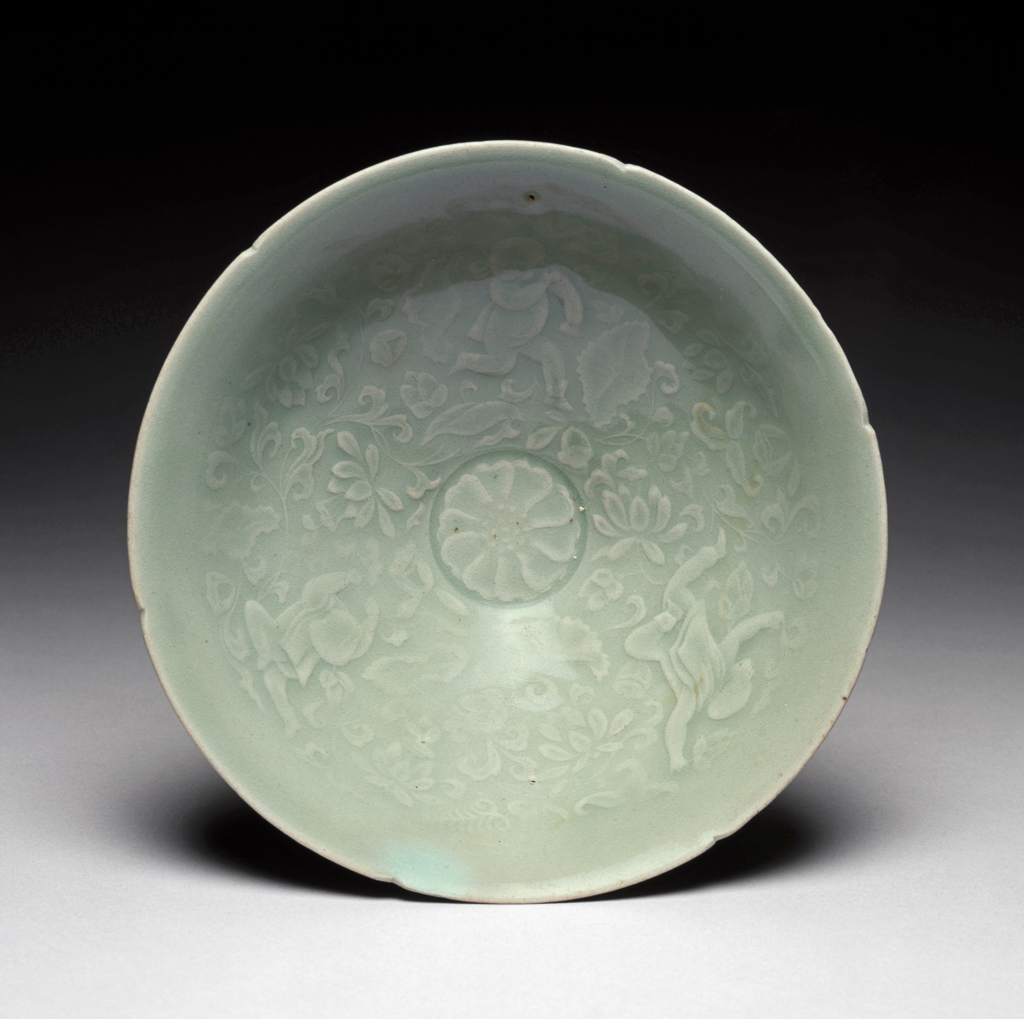 An image of Bowl with boys among lotus design. Unknown pottery, Korea, South Cholla province, Kangjin-gun, Sadang-ri kilns. This conical bowl has six indentations in the rim, suggesting a flower-like shape. The footring is low, the outside is plain, and the inside is finely moulded in shallow relief with a chrysanthemum flower-head in the centre and three boys playing among scrolling lotus round the sides. The pale bluish-green jade-like glaze is evenly applied, with a subtle gloss and no crackle. The base shows three neat quartzite spur-marks. Stoneware, thrown, moulded and celadon-glazed. Height, bowl, 6.7 cm, diameter, rim, 18.9 cm, diameter, foot, 6.2 cm, circa 1100-1150. Koryo Dynasty.