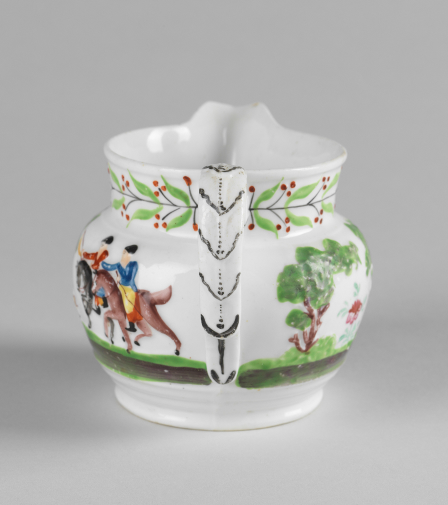 An image of Jug.  New Hall Porcelain Factory, Staffordshire, New Hall. With a hunting scene and a leaf and berry border painted in polychrome enamels. The bulbous jug stands on a low foot, and has a short cylindrical neck with a projecting lip. The strap handle is moulded with leaves in relief, and has a projecting finger rest near the lower end. On the sides, two men on horseback are galloping to the left towards a deer attacked by hounds beside a tree, and another man on foot who is brandishing a whip in one hand and holds the reigns of his horse in the other. On the other side is his horse trotting to the right, and behind it, two trees with a stylized flowering plant between them. Round the neck there is a continuous black stem bearing paired green leaves and paired black stalks with three red berries on each. The leaves on the back of the handle are outlined in black and have black dotted central vein. Bone china, moulded with decoration in relief, painted overglaze in blue, green, yellow, red, brown and black enamels, height, whole, 8.5 cm, length, whole, 12.5 cm, circa 1818-1825.