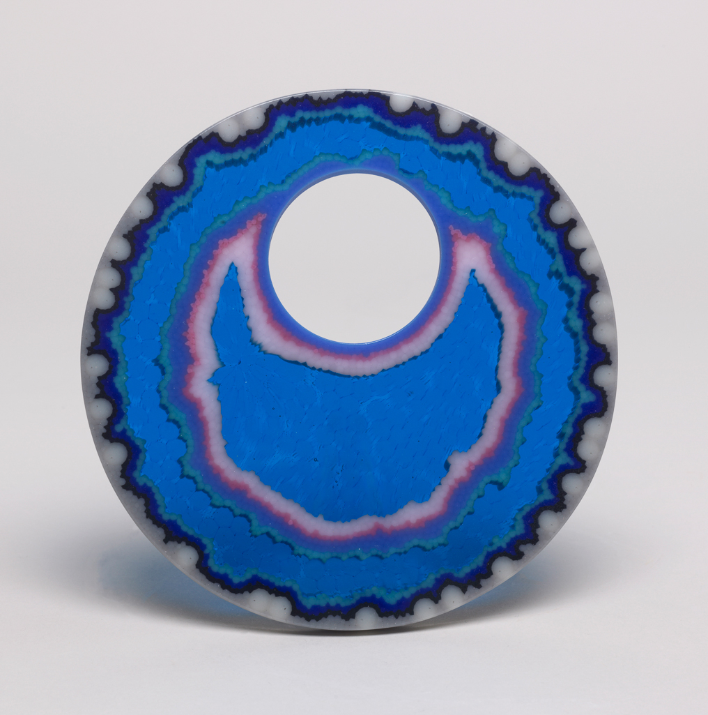 An image of Studio Glass/Cast Glass. Vessel. Cobalt Blue Agate Geode. Jarman, Angela (British, b. 1971). Cobalt blue lead crystal vessel, produced by lost wax casting, with mixed blue murrini cover. The vessel has a near-spherical shape with a wide mouth. The outside is polished; the interior is multifaceted with a rough surface; the walls are thick with an indented rim around the mouth to hold the insert; the underside is flat, circular and polished. The insert is a smooth, flat disc, with an off-centre circular hole, coloured with irregular, roughly concentric bands of fused opaque grey, blue, turquoise, pink and red glass. Between the bands and in the centre are wider areas of translucent cobalt blue glass, in which cell-like forms can be seen.  Lead crystal, cast and polished, with mixed blue murrini insert. Height, whole, 12.5 cm, diameter, 20 cm, 2017. Production Note: Murrini, glass mosaic that resembles agate stone, is characterised by fusing together differently coloured glass into concentric streaks, typically of purple and white. The process was known in Roman times and rediscovered by Venetian glass-makers in the 16th and 19th centuries. Acquisition Credit: Given by Nicholas and Judith Goodison through The Art Fund.