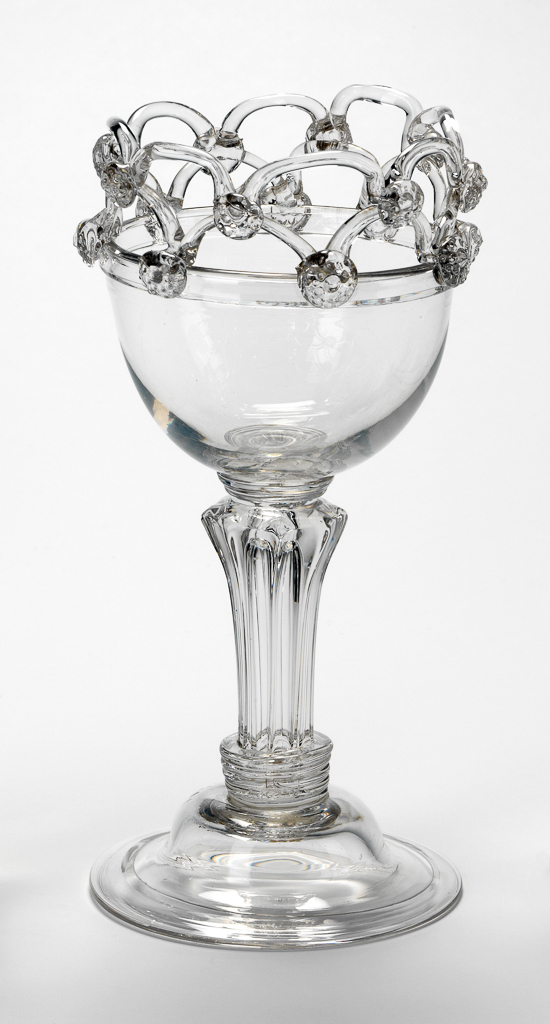 An image of C.614-1961: Sweetmeat glass/dessert glass. Unknown English glassmaker. Moulded double-ogee bowl, looped rim with prunts on triple collar and simple white opaque twist stem, domed and folded foot, moulded to match bowl. Lead-glass, bowl and foot moulded, height, whole, 16.5 cm, diameter, whole, 8.9 cm, circa 1760. Adlib numbers of others to be confirmed. One posset pot on left, engraved drinking glass on right.