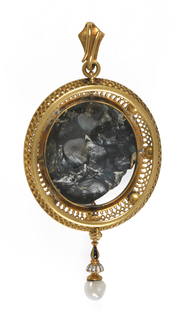 An image of Jewellery. Pendant. Unknown frame maker, London. Giuliano, Carlo, cameo maker (Italian jeweller in GBR, 1831-1895). Onyx cameo with white upper layer and dark lower layer, carved with a head of Medusa of Rondanini type. Shown frontally, the back left rough. Set by means of seven claws in an oval gold openwork frame enamelled black and white and set with four pearls and four cobochon pink gemstones. Suspended from the lower edge are a pearl, and an enamelled gold 'tassel' with a larger pearl at the end. At the top there is a ring and an enamelled gold loop for suspension. Height, whole, 8.2 cm, width, whole, 3.8 cm, height, cameo, 2.5 cm, width, cameo, 2.6 cm, depth, cameo, 0.9, cm, circa AD 100-200, cameo, mount late 19th century. Revivalism. Production Note: This pendant unites a second century Roman Imperial cameo of Medusa with a Renaissance Revival style mount, by Carlo Giuliano one of the leading jewellers who worked in both the Renaissance and Archeological Revival styles.