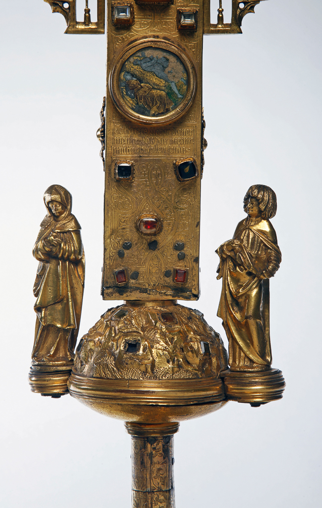 An image of Sculpture. Crucifix/altar cross. Sexfoil engraved with the Resurrection; the angel with the two Maries at the tomb; Noli me tangere; the walk to Emmaeus; the Ascension; and Pentecost. The cross, which contains a reliquary, is set with imitation stones, and enclosed in canopy work among which are the figures of the twelve apostles, and the central figure of the donor, or the saint to which the church was dedicated. There is an angel at either end of the cross-bar, both holding a chalice. There are four circular medallions of enamel on the front of the cross. Top: St. Luke with the bull; right St. Mark with the lion; left: St. John with the eagle; bottom: Adam and Eve expelled from the garden of Eden. (?St. Matthew at the top and missing, as the plaque of the Expulsion should be on the reverse of the cross). Beneath the Expulsion are the words: 'Johanesz hieber diener/meinn. Lasz dir meinn/mütter befollen seinn.' (John, I herewith commend my mother to you.') which refers to the figures of the Virgin Mary and St. John who are standing at the foot of the cross. [The Virgin on the left and St. John on the right]. The three enamel medallions on the back of the cross are; top: Creation of Eve from Adam's side; left: Eve tempting Adam with the apple; right: Adam and Eve hiding from the Lord God in the garden. The fourth medallion is missing, and it may be suggested that the Expulsion should belong here. Engraved at the top of the back of the cross is God the Father and Creator, crowned with a Jewish high-priestly mitre (or the imperial crown?), and holding an orb and a sceptre terminating in a fleur-de-lis. Below, on the cross-bar, is the garden of Eden with many animals (which perhaps represent unfallen nature). Below this again is the scene from Numbers XXI. Here a man lies bitten by a snake, in front of the tents of the camp of the Israelites, while Moses, with two horns upon his head stands by. There is a reliquary compartment behind the figure of Christ, crowned with 