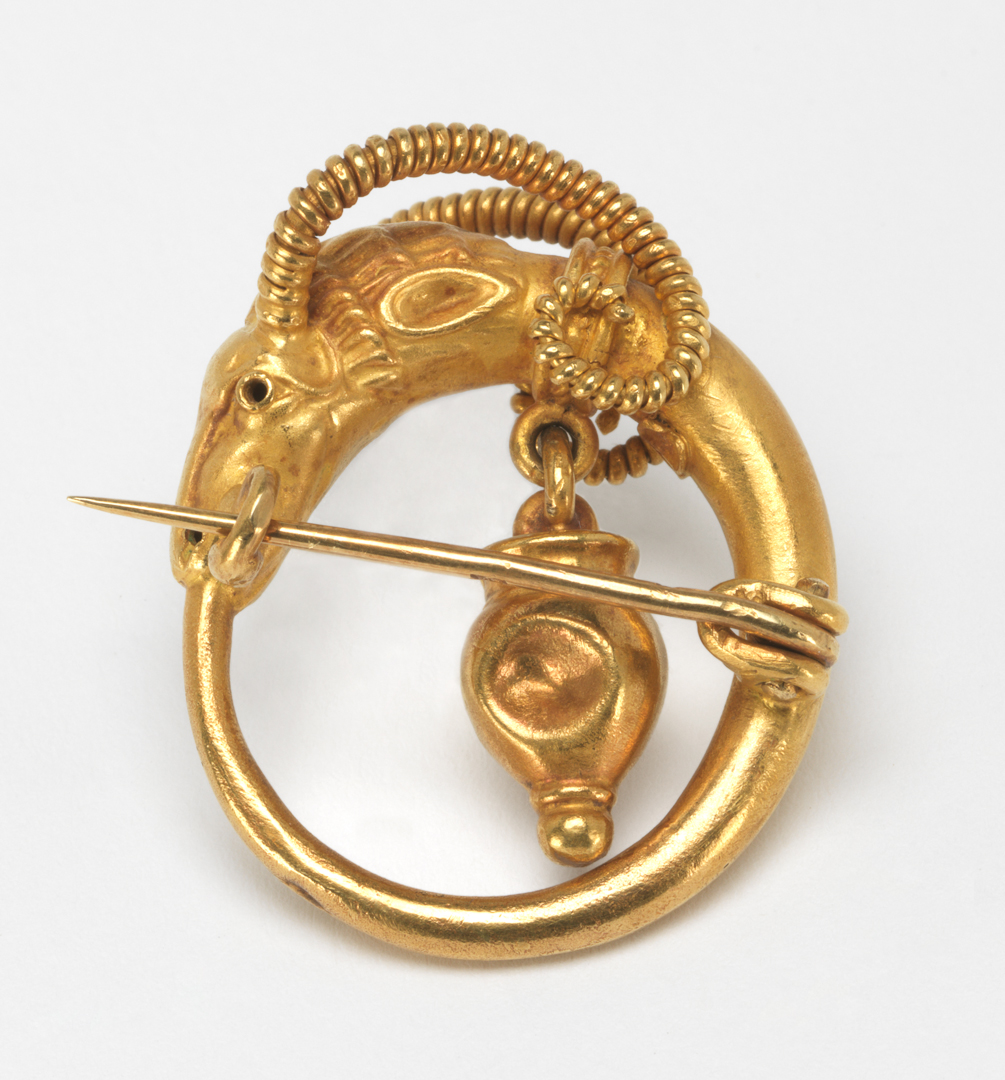 An image of Jewellery. Brooch cast in the shape of a ring with an antelope or gazelle’s head at the top, which has a vase suspended inside the ring from its collar. Castellani family, (Italian, 19th-20th centuries). Pin fastening across the back. Gold, cast, height, whole, 3.3 cm, width, whole, 3.1 cm, circa 1860-1870. Archaeological Style. Acquisition Credit: Given by Mrs J. Hull Grundy.