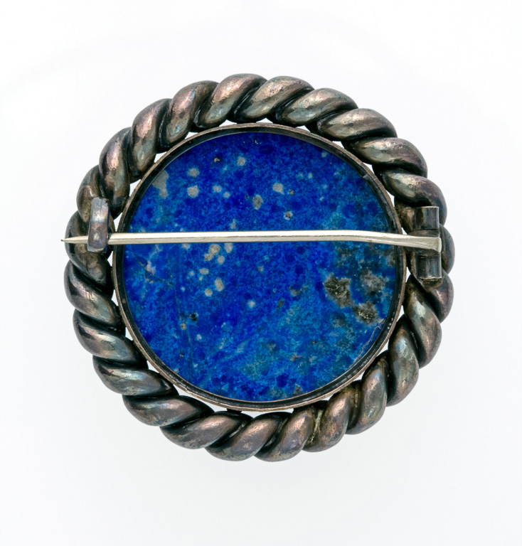 An image of Lapis lazuli and silver brooch. Stein, Michael (possibly); Stein, Leo probably (1872-1947). Cabochon lapis lazuli with pyrite and calcite inclusions, in a circular silver setting with a twisted 'rope' border; pin fastening across the back, diameter 4.2 cm, circa 1900. Made in Colmar, Paris.