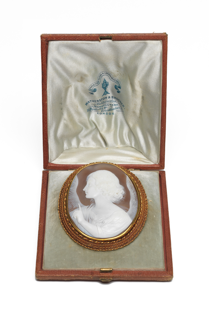 An image of Jewellery. Brooch. Shell cameo mounted in gold. Watherston & Brogden, England. Cameo bust of an angel in profile to the left with the index finger of its left hand raised, mounted in gold and surrounded by a border of four strands of gold ropework; pin-fastening across the back. In original red leather case (A), the lid of which is lined with white silk, printed in blue with the maker's name and adress: 'PARIS FIRST CLASS & LONDON PRIZE MEDALS/Watherston & Brogden/ Goldsmiths/ MANUFACTORY/16 Henrietta St/Covent Garden.WC/LONDON'. Gold, shell, height 7.21 cm, width 5.9 cm, 1862-1864. Victorian. Acquisition Credit: Given by Mrs J. Hull Grundy.