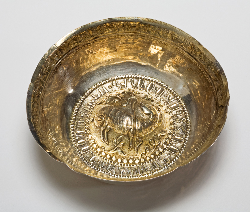 An image of Bowl. Wine Cup/Wine Taster. Unknown silversmith, Balkans, possibly. No hallmarks or maker's marks. The bowl has an everted rim and domed base. The rim is gilt and chased with a border of stylised flowers on a matted ground, beneath is a punched border. The base is gilt and embossed with an Agnus Dei; the stylised lamb on a matted ground embossed with leaves and a border of beads, and surrounded by a Cyrillic inscription. Silver, parcel-gilt, raised, embossed, chased, matted and punched, height, to rim, 3.5 cm, approximate, diameter, across rim, 11.3 cm, approximate, weight, whole, 62 g.