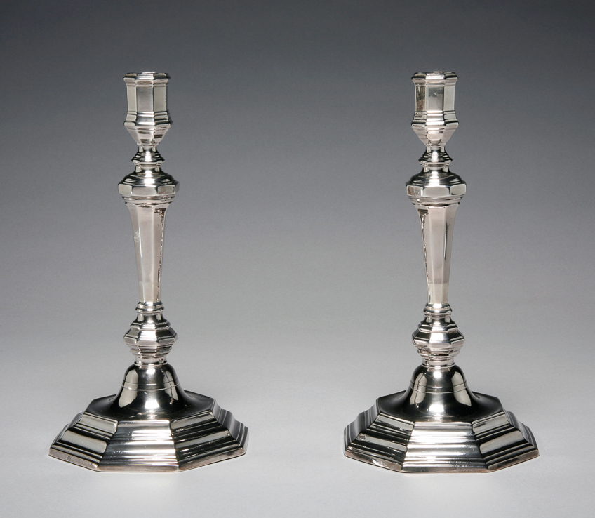 An image of A pair of candlesticks. Grebeude, N., silversmith, France, Paris, Colmar. Of octagonal form. The urn-shaped sconce on a slender vase-shaped column over a flattened knop, stands on a slightly domed base with stepped octagonal foot. Silver, cast, height, overall, 25.2 cm, width, base, 13 cm, weight, whole, 595 g, 1723-1724. Régence. Louis XV.