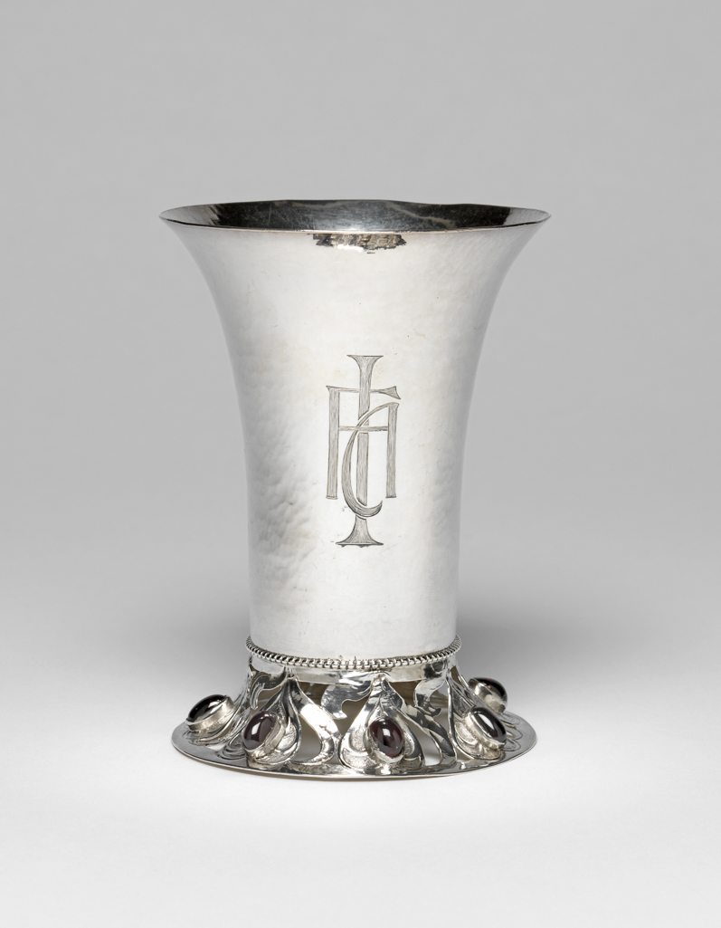 An image of Silverware. Beaker/Drinking Vessel. Ashbee, Charles Robert (British, 1863-1942). Silver beaker with hammered surface, the foot pierced, chased, and set with unbroken amethysts. Maker’s mark of C.R. Ashbee and London hallmarks. After 1900 to before 1901. Acquisition Credit: Given by the estate of the late Olive and Peter Ward. Former loan number; AAL.6-2005.